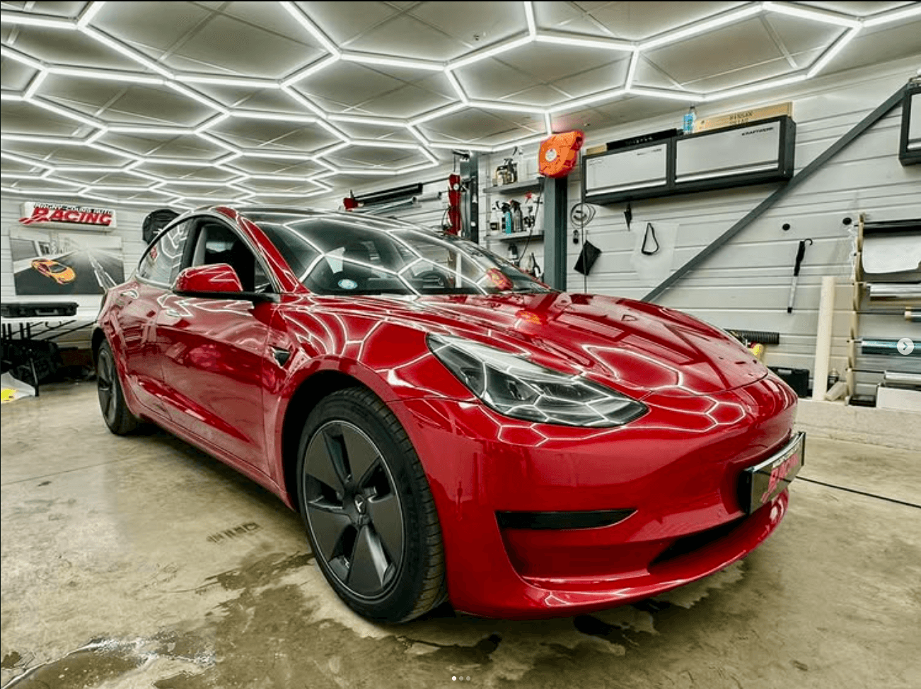 Tesla Model 3 rouge dans l'atelier AWD Magny-Cours sous l'éclairage hexagonal, capot protégé par film XPEL Ultimate avec traitement céramique Fusion Premium V2
