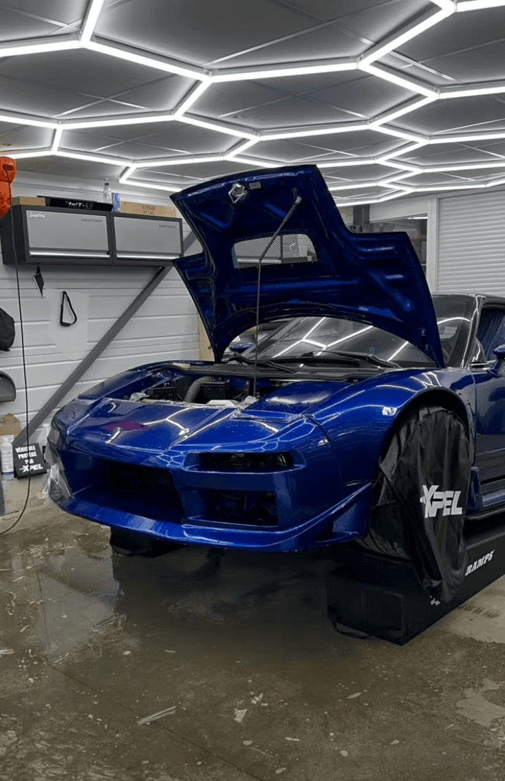 Honda NSX bleue en cours de protection PPF XPEL dans l'atelier AWD Magny-Cours, capot ouvert sous l'éclairage hexagonal